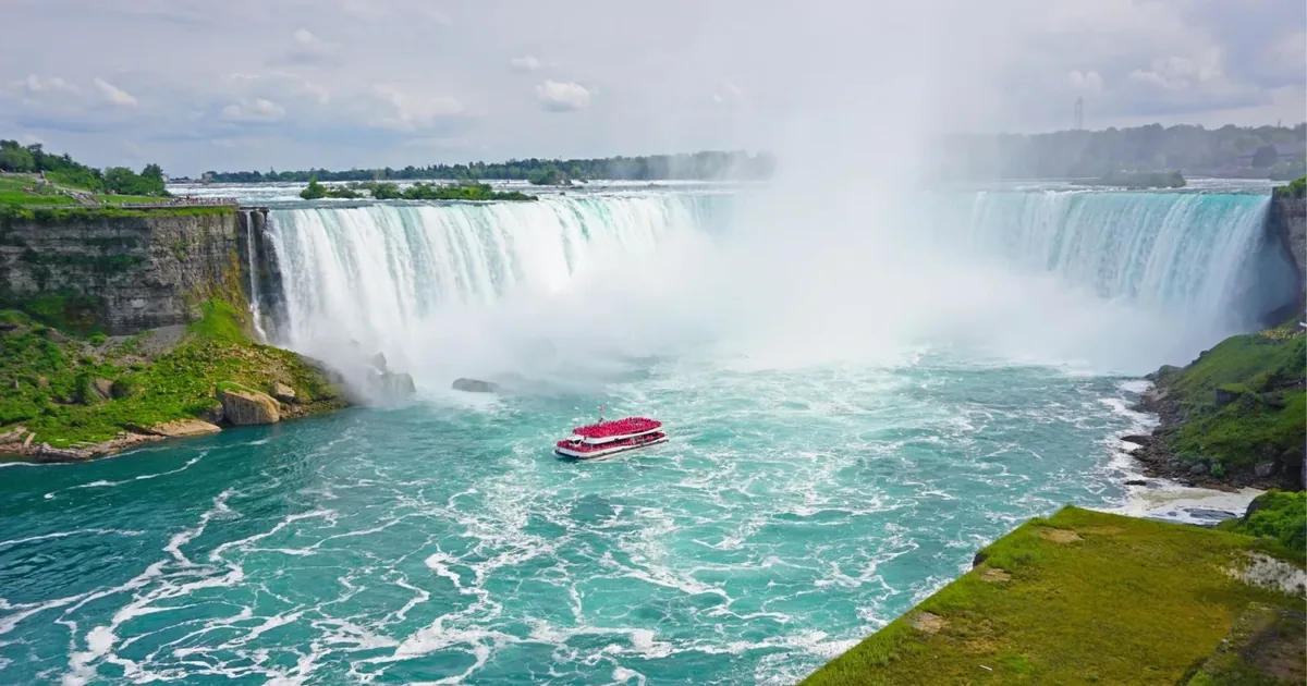 Niagara Falls tour boat full of passengers in red ponchos in the turquoise basin below Horseshoe Falls