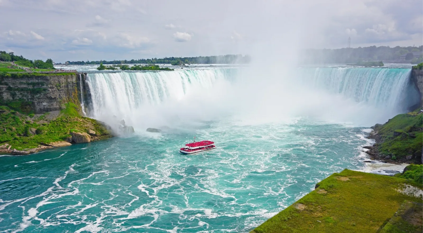 Horseshoe Falls seen wide from the Canadian side, a cruise boat full of red-ponchoed passengers in the turquoise basin below