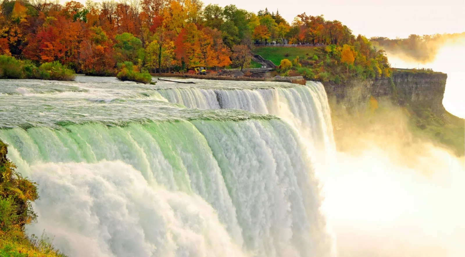 American Falls in autumn, orange and red maples lining the rim above the green crest of the water