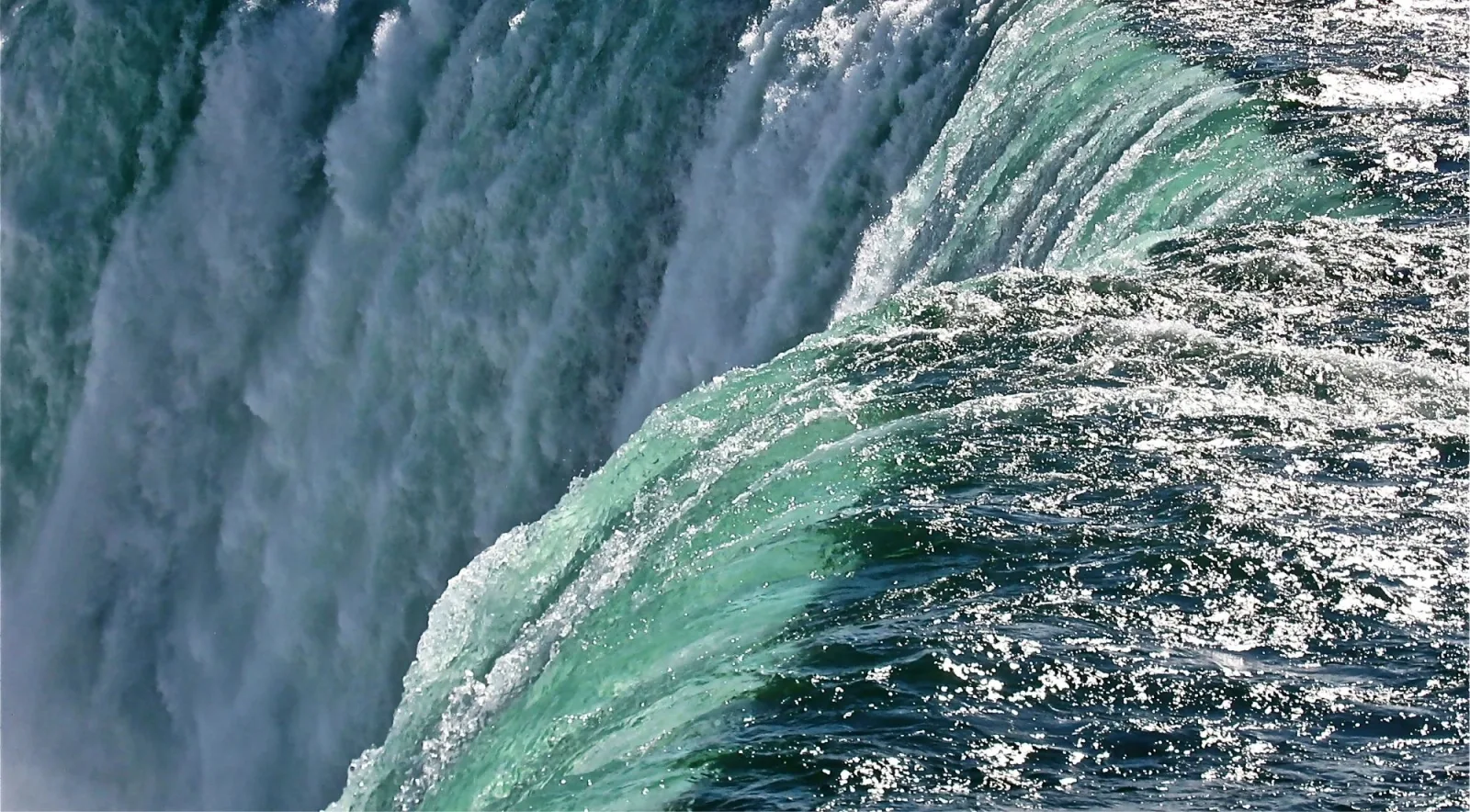 Close view of the green crest of Niagara Falls curling over the edge beside the falling white water