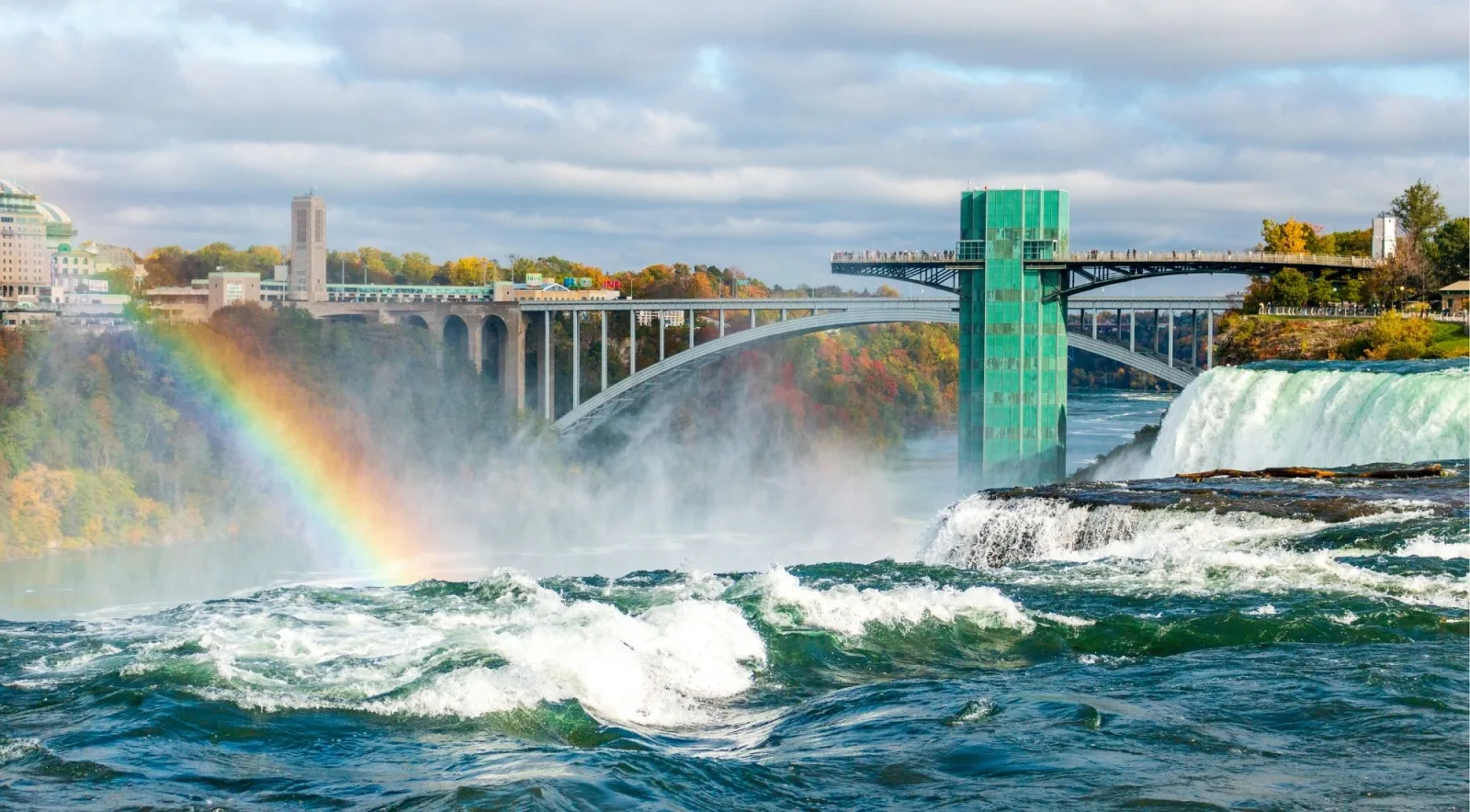 Rainbow arcing over the Niagara Gorge beside the Rainbow Bridge, with rapids running in the foreground