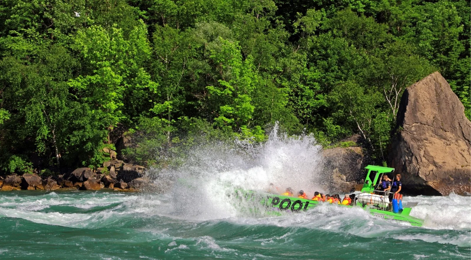 Bright green Whirlpool jet boat burying its bow in a standing wave on the Niagara River, riders in orange life vests behind the spray