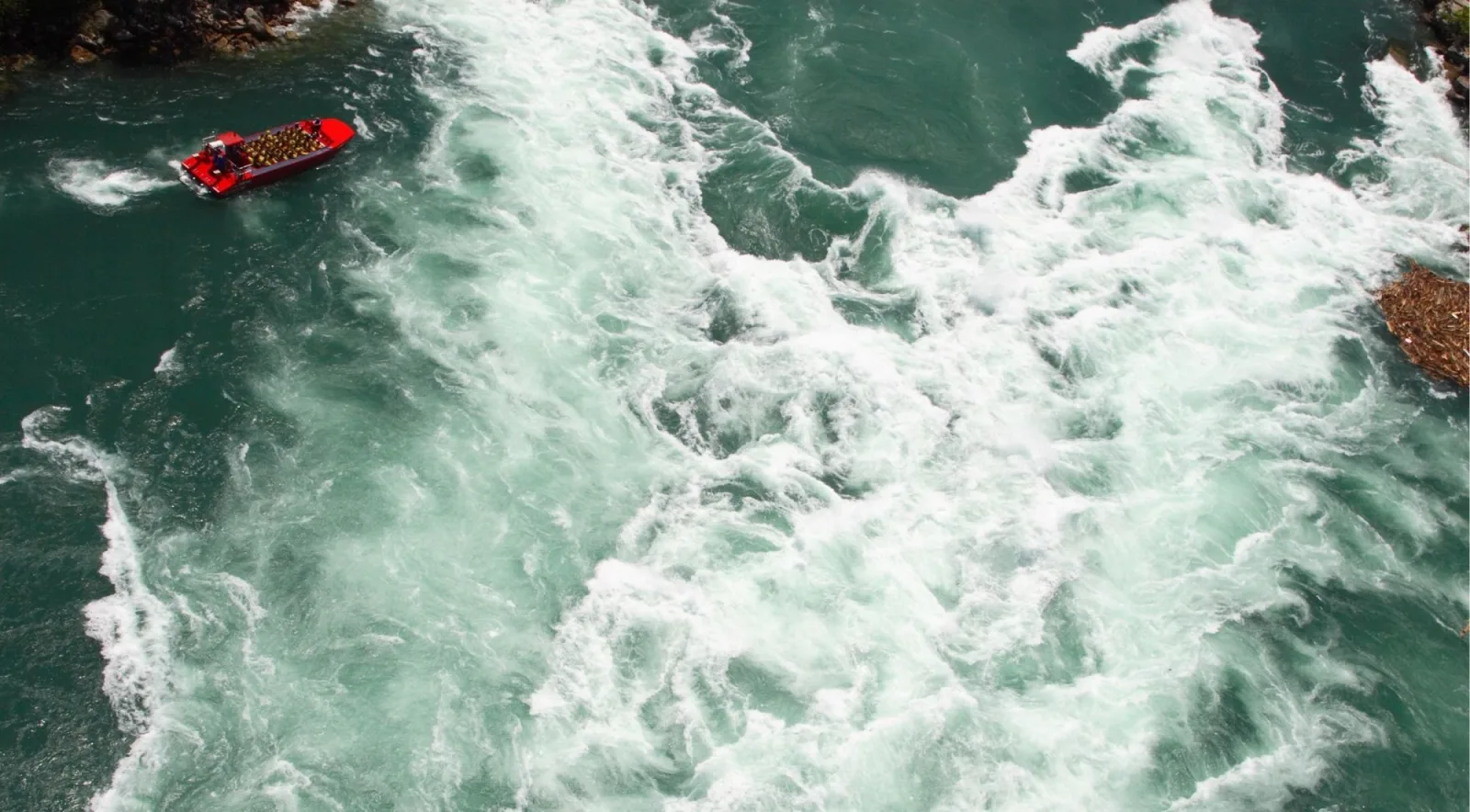 Aerial view of a red jet boat idling at the edge of the churning Whirlpool Rapids on the Niagara River
