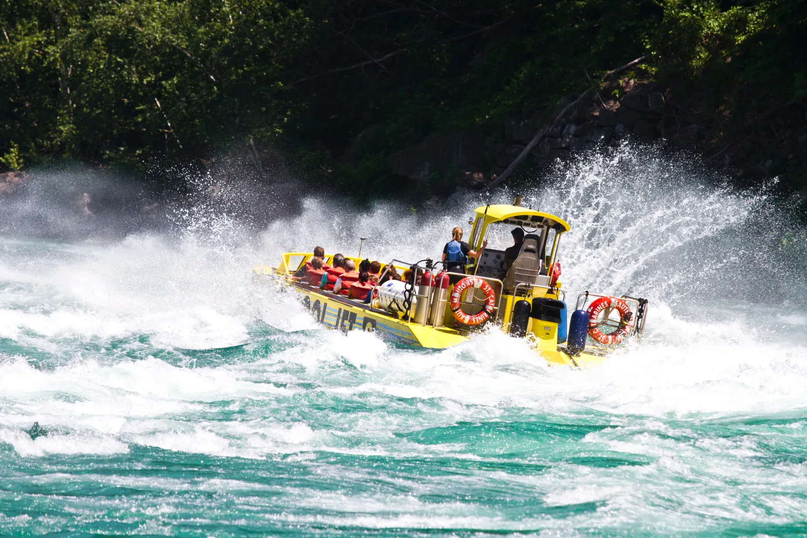 Yellow open jet boat throwing twin walls of whitewater as it powers through the Niagara rapids