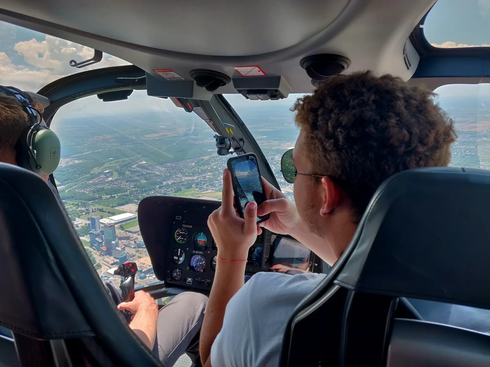 A passenger filming on a phone from the rear seat, the pilot at the controls and the instrument panel visible ahead
