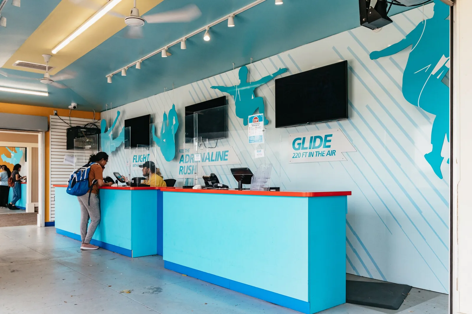 The zipline check-in counter, its wall painted with figures in flight and a sign reading Glide 220 ft in the air