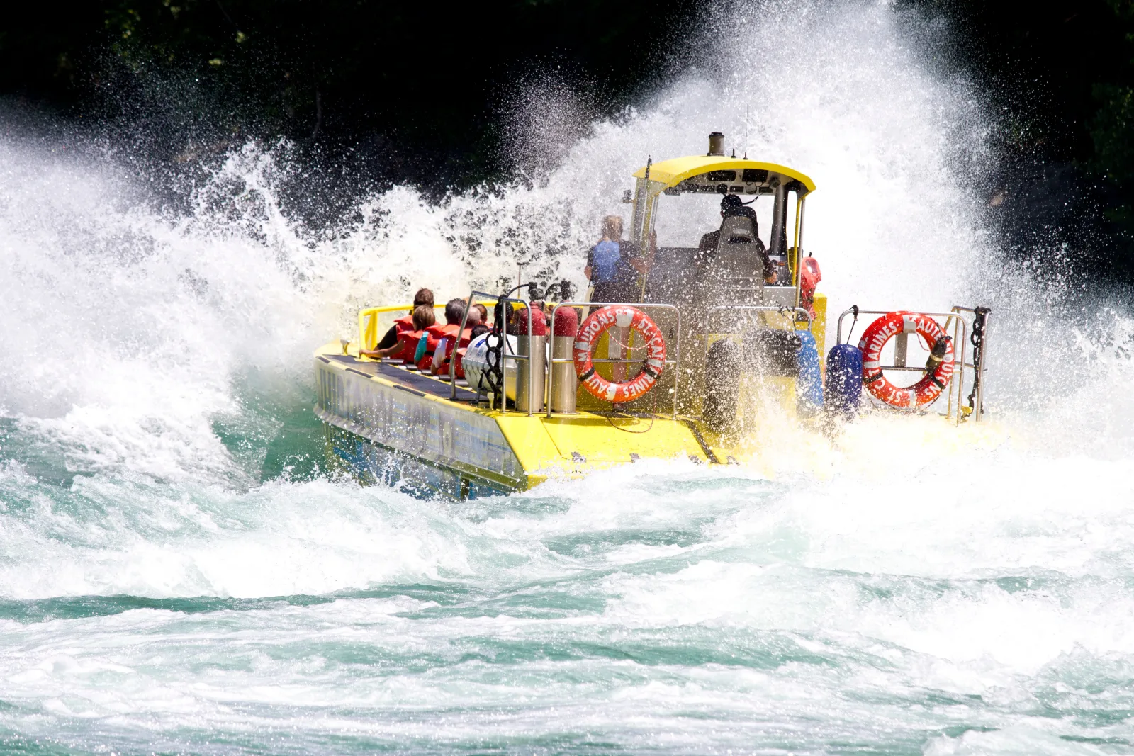 Yellow open jet boat almost lost inside an explosion of whitewater in the Niagara Gorge, life rings and riders just visible through the spray