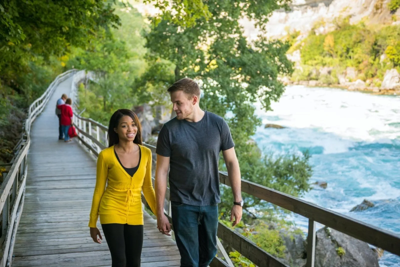 A couple walking the White Water Walk boardwalk beside the Niagara Gorge, whitewater running below the rail on their right