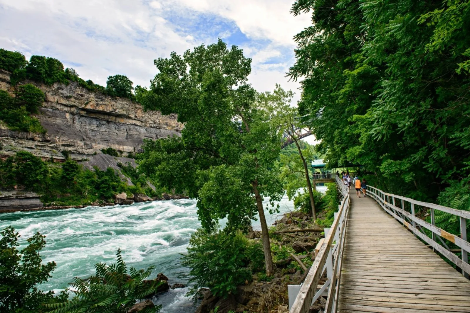 The White Water Walk boardwalk curving along the base of the Niagara Gorge beneath layered limestone cliffs, rapids running alongside