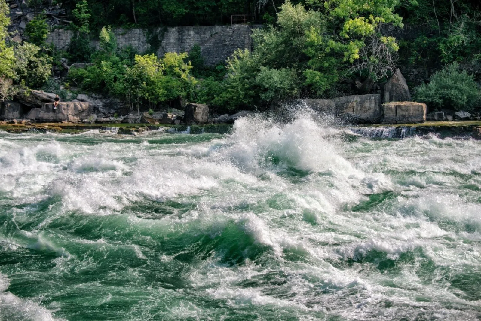 Class 6 whitewater surging past the gorge wall, standing waves breaking well above head height beside the boardwalk