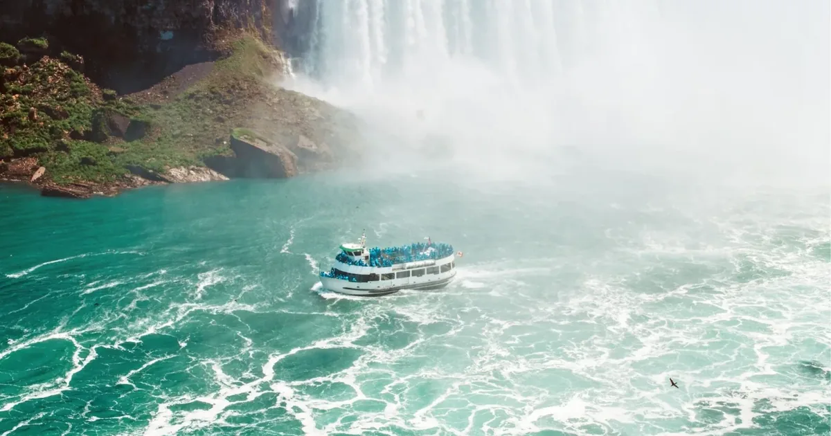 Niagara City Cruises boat crowded with passengers in ponchos turning in the emerald water at the foot of Horseshoe Falls