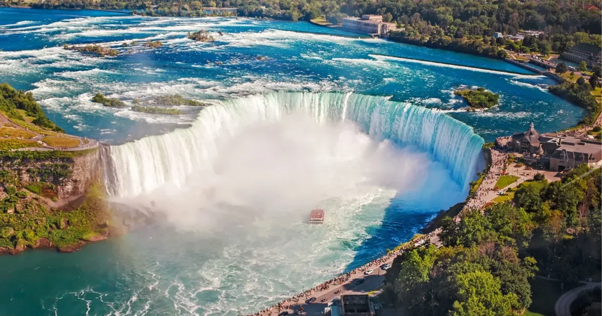 Aerial view of Horseshoe Falls with the Niagara River above it and the Canadian promenade crowded along the rim