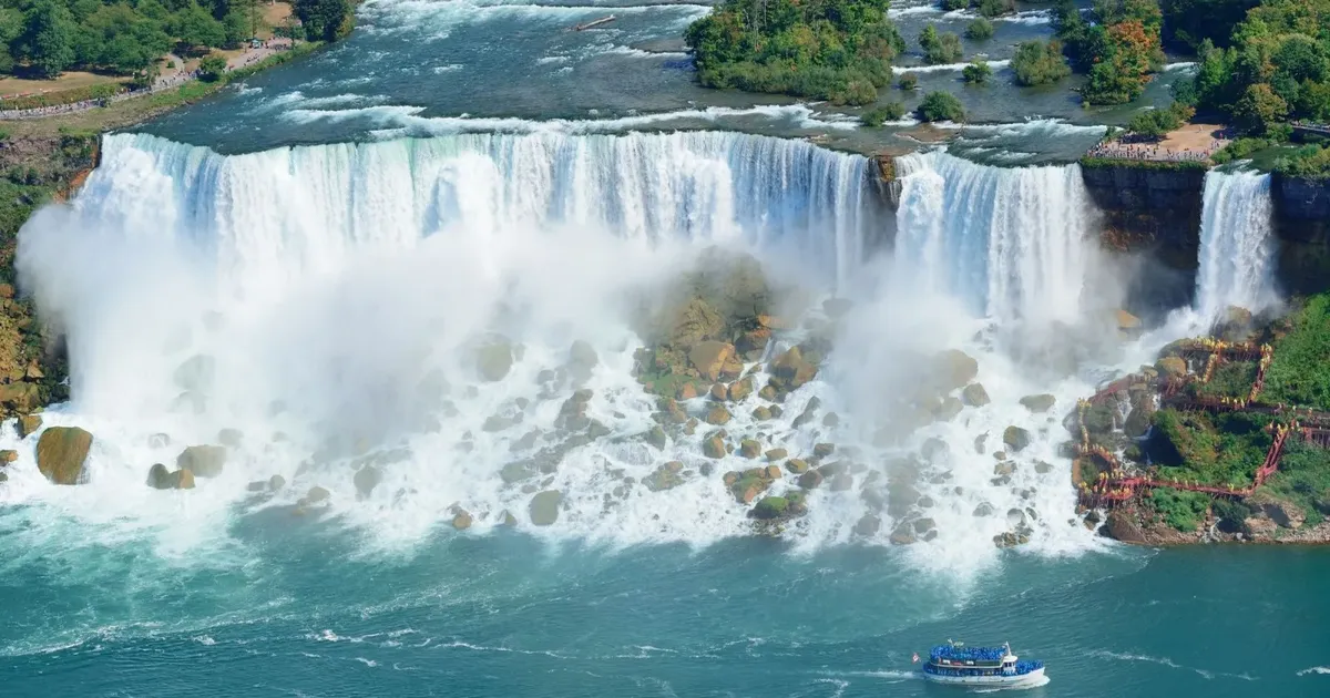 Aerial view of the American and Bridal Veil Falls with the red Cave of the Winds walkways at the foot of the falls and a Maid of the Mist boat crossing the river below